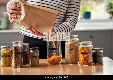 Donna che risparmia sul packaging riempiendo vasi riciclati per conservare cibo essiccato a casa Foto Stock