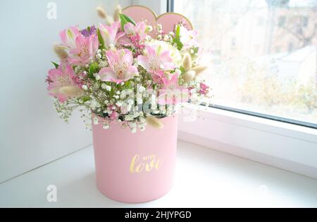 Delicato bouquet di gigli rosa, rose bianche e gypsophila in una scatola regalo parola d'amore sulla finestra. Foto Stock