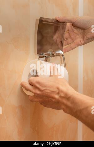 la mano maschio installa un nuovo rotolo di carta igienica nel supporto. Foto di alta qualità Foto Stock