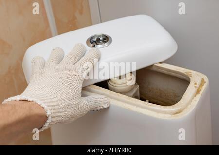 la mano di un uomo in un guanto apre il coperchio del serbatoio di risciacquo del gabinetto. Foto di alta qualità Foto Stock