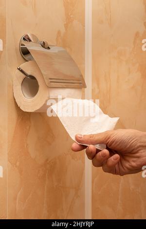 la mano dell'uomo strappa un pezzo di carta igienica nel gabinetto. Foto di alta qualità Foto Stock