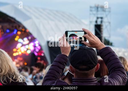 Una persona che usa un telefono cellulare per video la band che suona sul palco in un grande festival musicale in un parco in Essex. Registrazione dello spettacolo Foto Stock