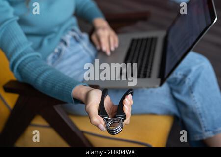 Lavoratore di ufficio femminile che utilizza un computer portatile e comprime il simulatore di espansore carpale regolabile a mano Foto Stock