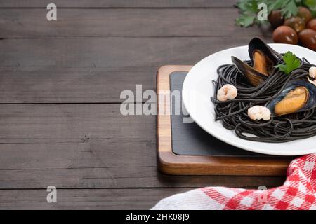 Piatto di pasta nera con frutti di mare su sfondo di legno con copyspace. Concetto di cucina mediterranea. Foto Stock