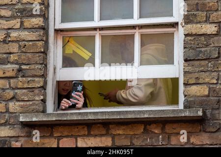 Londra, Regno Unito. 1 febbraio 2022. La gente guarda fuori da una finestra per vedere il Principe di Galles e la duchessa di Cornovaglia a Chinatown per celebrare il Capodanno lunare, l'anno della Tigre con una visita ai negozi, alle organizzazioni e alle comunità locali. Credit: Stephen Chung / Alamy Live News Foto Stock