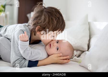 Due bambini, baby e suo fratello nel letto la mattina, giocare insieme, ridendo e avente una buona volta, la condivisione di un momento speciale, incollaggio Foto Stock