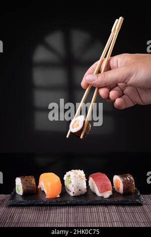 Selezione manuale di sushi varietà con chopstick su sfondo scuro. Formato verticale. Foto Stock