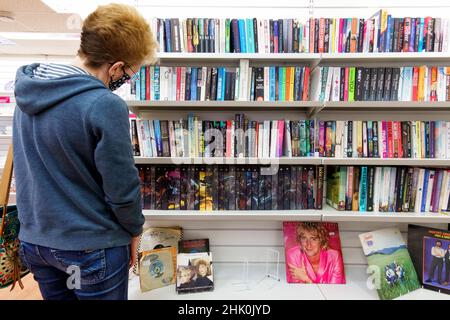 Una cliente femminile esplora una selezione di donazioni di libri di seconda mano sugli scaffali in un locale High Street, PDSA Charity Shop del Regno Unito Foto Stock