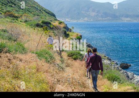 La gente cammina e si arrampica attraverso l'ambiente naturale con cespugli e ripide formazioni rocciose in Monemvasia Grecia. Scena con il cielo blu e il Mar Mediterraneo Foto Stock