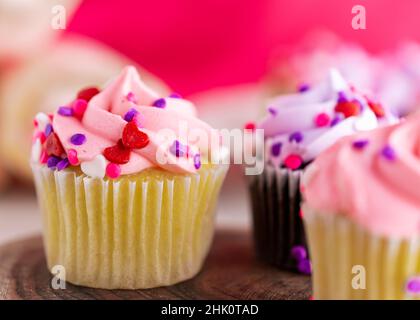 Una vista ravvicinata di un assortimento di mini cupcake di San Valentino su una lastra di legno. Sfondo rosa con una profondità di campo molto bassa. Foto Stock