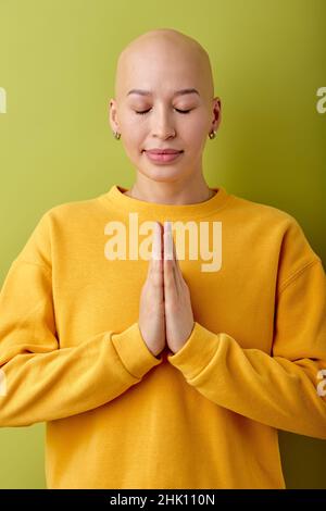 calmo e gorgeous giovane calvo caucasica donna con gli occhi chiusi che posano alla macchina fotografica, pregando. ritratto di graziosa signora in giallo casual camicia isolato sopra Foto Stock