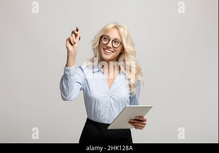 Giovane donna d'affari intelligente con scrittura di marcatori o disegno su schermo virtuale, in piedi su sfondo grigio chiaro Foto Stock