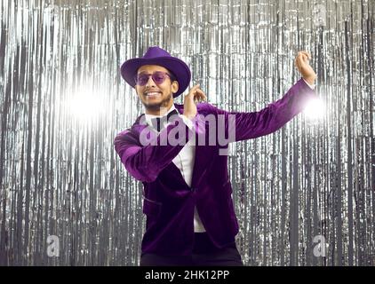 Buon ragazzo goofy indossando una divertente giacca viola e cappello ballare in una discoteca party Foto Stock