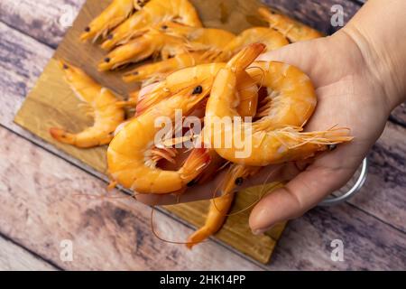 la mano di una donna tiene una manciata di gamberi bolliti sullo sfondo di un tavolo di legno Foto Stock