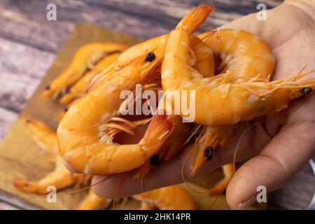 la mano di una donna tiene una manciata di gamberi bolliti sullo sfondo di un tavolo di legno Foto Stock