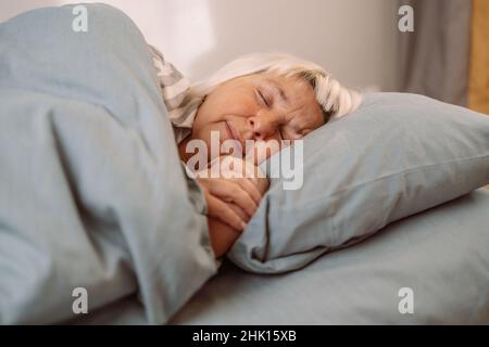 Sogni dolci. Bella 50s donna che dormiva a letto presto al mattino. Persone, relax e comfort concetto Foto Stock