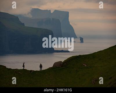 Le silhouette turistiche sullo sfondo di Risin og Kellingin rocce e scogliere di Eysturoy e Streymoy isole visto punto di vista vicino Kallur faro su t Foto Stock