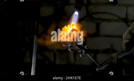 Il fabbro allinea le foglie di ferro rosa e fa la forma finale del fiore. Il fabbro fa rosa di ferro. Foto Stock