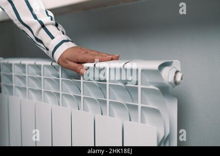 La mano femmina tocca un radiatore di riscaldamento a casa. Foto Stock