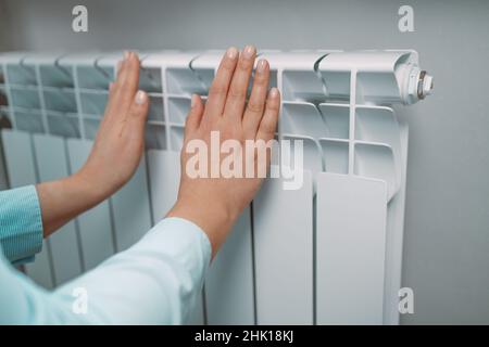 Le donne toccano la batteria appena calda durante la stagione di riscaldamento. Dispositivi di riscaldamento in casa, vista laterale Foto Stock