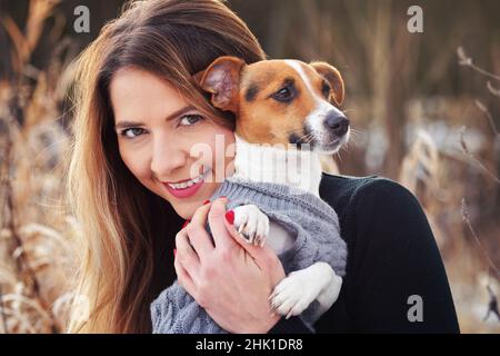 Giovane donna che tiene il suo cane terrier Jack Russell indossare abiti invernali caldi sulle mani Foto Stock