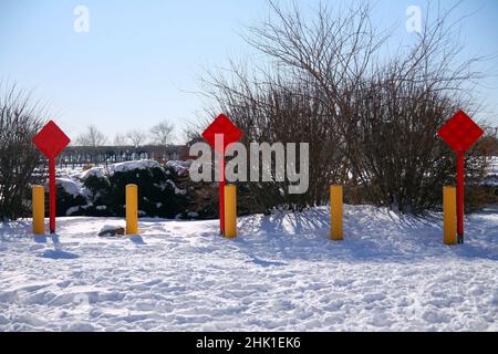 Fine rossa della strada segno quadrato con tre pali gialli sulla neve in una giornata di sole dopo una tempesta Foto Stock