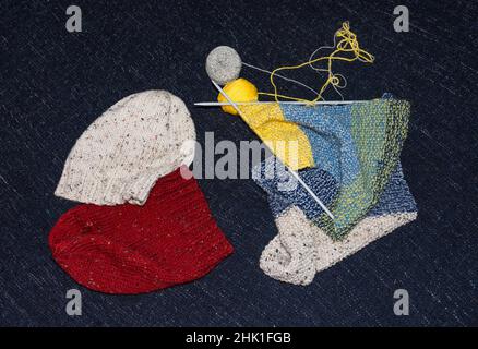 Nel processo di lavorazione a maglia, attrezzatura per maglieria, aghi e lana accanto ai cappelli a maglia, vista dall'alto Foto Stock