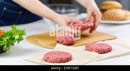 Mano della donna che forma una carne di manzo per una festa di hamburger. Porzionamento carne macinata. Hamburger fatti in casa. Fare il cibo a casa. Foto Stock