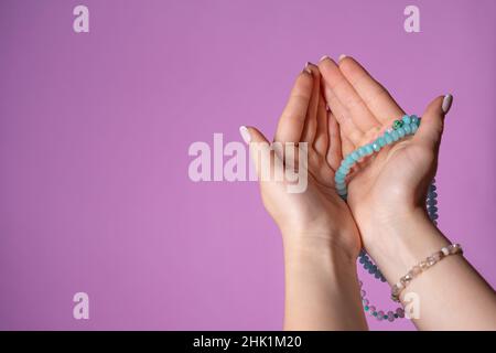 La donna tiene in mano il rosario o il filamento di perle di mala usato per mantenere il conteggio durante le meditazioni di mantra. Preghiere. Apri le palme con gratitudine. Sfondo rosa Foto Stock