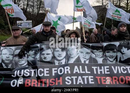 Derry, Regno Unito. 30th Jan 2022. Un gruppo di manifestanti marcia con bandiere che sventolano e una bandiera che legge ''Giustizia per le vittime del terrorismo di Stato britannico!?' Durante la passeggiata ricordo per onorare le vittime. Il 30 gennaio 1972, il reggimento paracadute dell'esercito britannico ha sparato e ucciso 14 civili. Le famiglie delle vittime, i locali, i sostenitori e i politici commemorano il 50th° anniversario della domenica di sangue a Derry. Il primo ministro irlandese, MicheÃl Martin, deputato al Parlamento Mary Lou McDonald, e Simon Coveney, ministro degli Affari esteri dell'Irlanda, hanno tutti partecipato all'evento di quest'anno Foto Stock