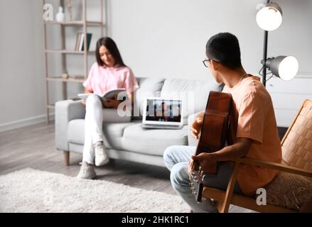 Giovane uomo che ha una lezione di chitarra online a casa Foto Stock