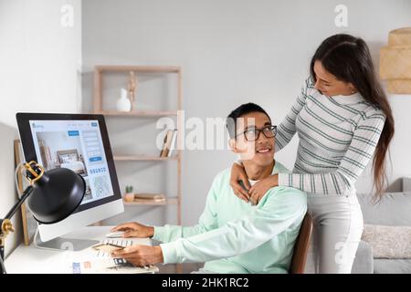 Giovane uomo con sua moglie che prenota una camera d'albergo online a casa Foto Stock