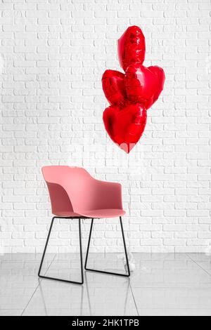 Sedia e palloncini d'aria a forma di cuore per San Valentino vicino a muro di mattoni bianchi Foto Stock