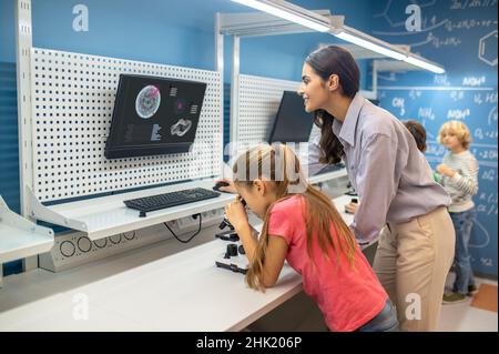 Donna che guarda la scheda di ricarica e ragazza vicino al microscopio Foto Stock
