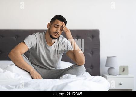 Concetto di fatica. Giovane uomo arabo stanco seduto a letto a casa Foto Stock