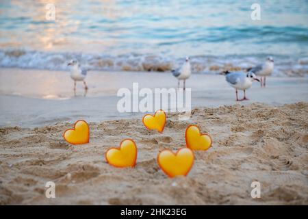 uccelli e cuori gialli nella sabbia si ergono sul mare Foto Stock