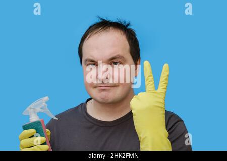 Uomo felice pulitore mostrando gesto di successo in guanti gialli, ritratto su sfondo blu studio Foto Stock