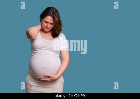 Dolore al collo in donna incinta, scatto in studio su sfondo blu Foto Stock