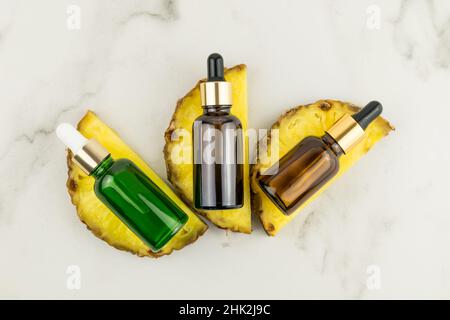 versare il siero con l'estratto di ananas o l'olio cosmetico in bottiglie con una pipetta sulle fette di frutta. vista dall'alto. posa piatta Foto Stock