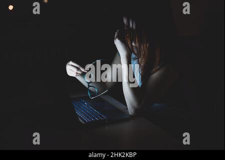 Donna con capelli rossi stanchi che lavora su un notebook. La ragazza al computer in disperazione tiene la mano sul ponte del naso. Guasto al lavoro. Scadenza e. Foto Stock