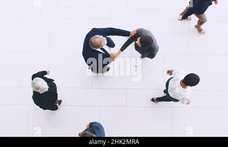 Diamo un'occhiata all'immagine più grande. Scatto corto di due uomini d'affari irriconoscibili che scuotono le mani mentre sono in ufficio con i loro colleghi durante il Foto Stock