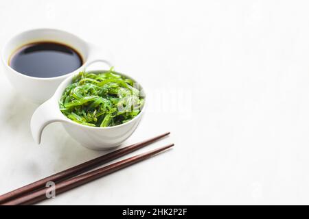 Wakame verde. Insalata di alghe e salsa di soia in ciotola su tavola bianca. Foto Stock