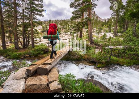 Backpacker che attraversa il torrente nel John Muir Wilderness, Sierra Nevada Mountains, California, USA. Foto Stock