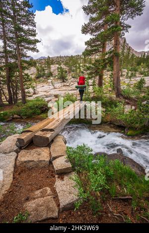Backpacker che attraversa il torrente nel John Muir Wilderness, Sierra Nevada Mountains, California, USA. Foto Stock