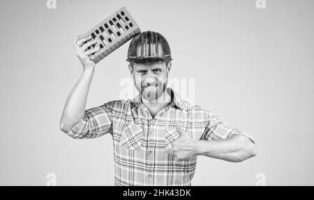 bel muratore uomo in caschetto di sicurezza e camicia a scacchi sul cantiere con mattoni, mattoni Foto Stock