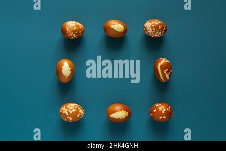 Uova decorate con cipolla biologica dipinge e foglie di piante in Pasqua. Telaio da uova. Sfondo blu. Vista dall'alto. Spazio di copia per il testo. Min Foto Stock