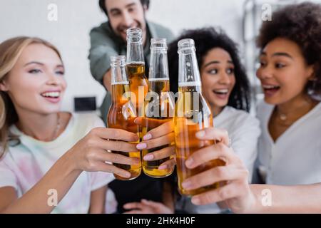 offuscato e felice gruppo interrazziale di amici che aggraffano bottiglie di birra Foto Stock