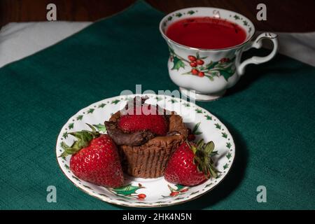 Coppette di Cheesecake al cioccolato doppio e fragole con stoviglie di frutti di bosco, una tazza di tè di Natale su un tovagliolo verde. Pugni nel teacup. Foto Stock