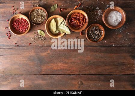 Varie spezie in piccole ciotole di legno su un rustico tavolo marrone, cibo e fondo di cottura, grande spazio copia, alto angolo di vista dall'alto Foto Stock