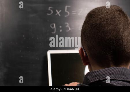 Il bambino con il laptop calcola davanti alla lavagna Foto Stock